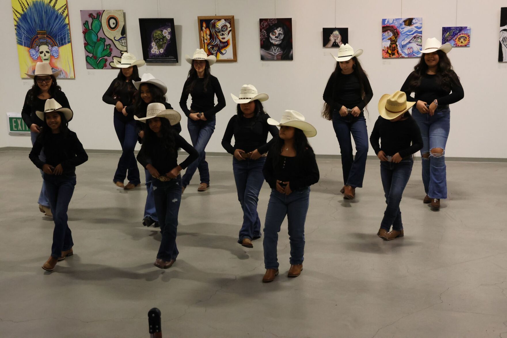 People dancing wearing hats and jeans with paintings in the background.
